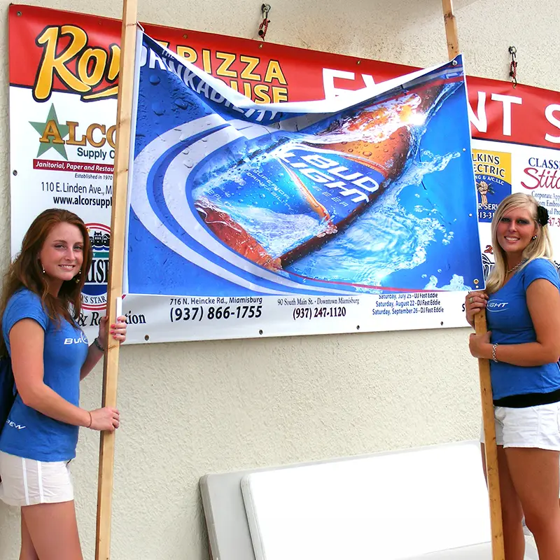 Downtown Festival-2009 Two women in blue shirts stand on either side of a promotional banner displaying a blue waterproof smartphone with water splashes.