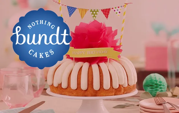Bundt cake with pink frosting and white drizzle sits on a plate, with pastel party decorations in the background.
