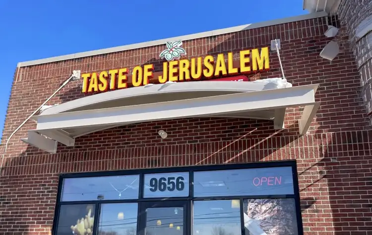Brick storefront with a bright yellow "TASTE OF JERUSALEM" sign above a white awning and glass doors.