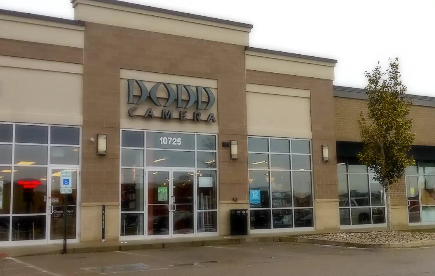 Front view of a strip mall storefront with a brick facade, large glass windows, and a sign above the central entrance.