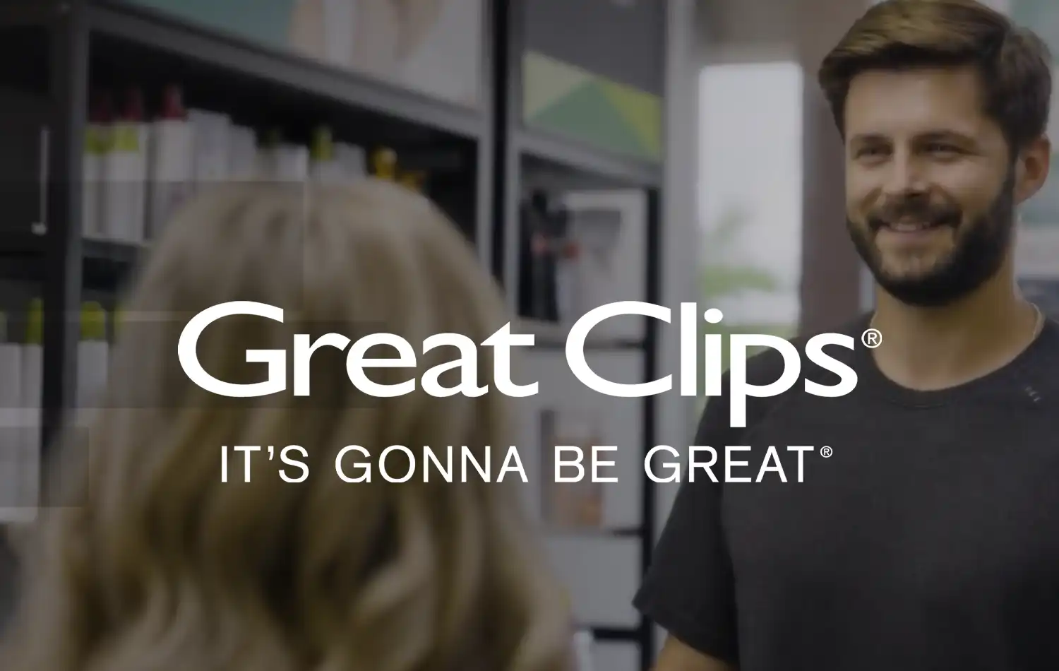 A smiling hairstylist chats with a customer in a Great Clips hair salon, with the Great Clips logo visible.