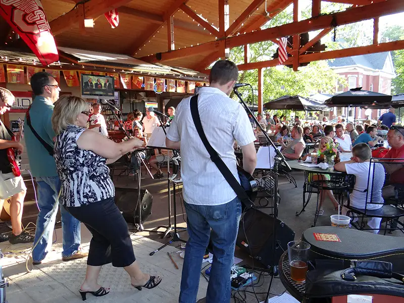 A live band performs on an outdoor stage while diners sit at tables under a wooden pavilion.