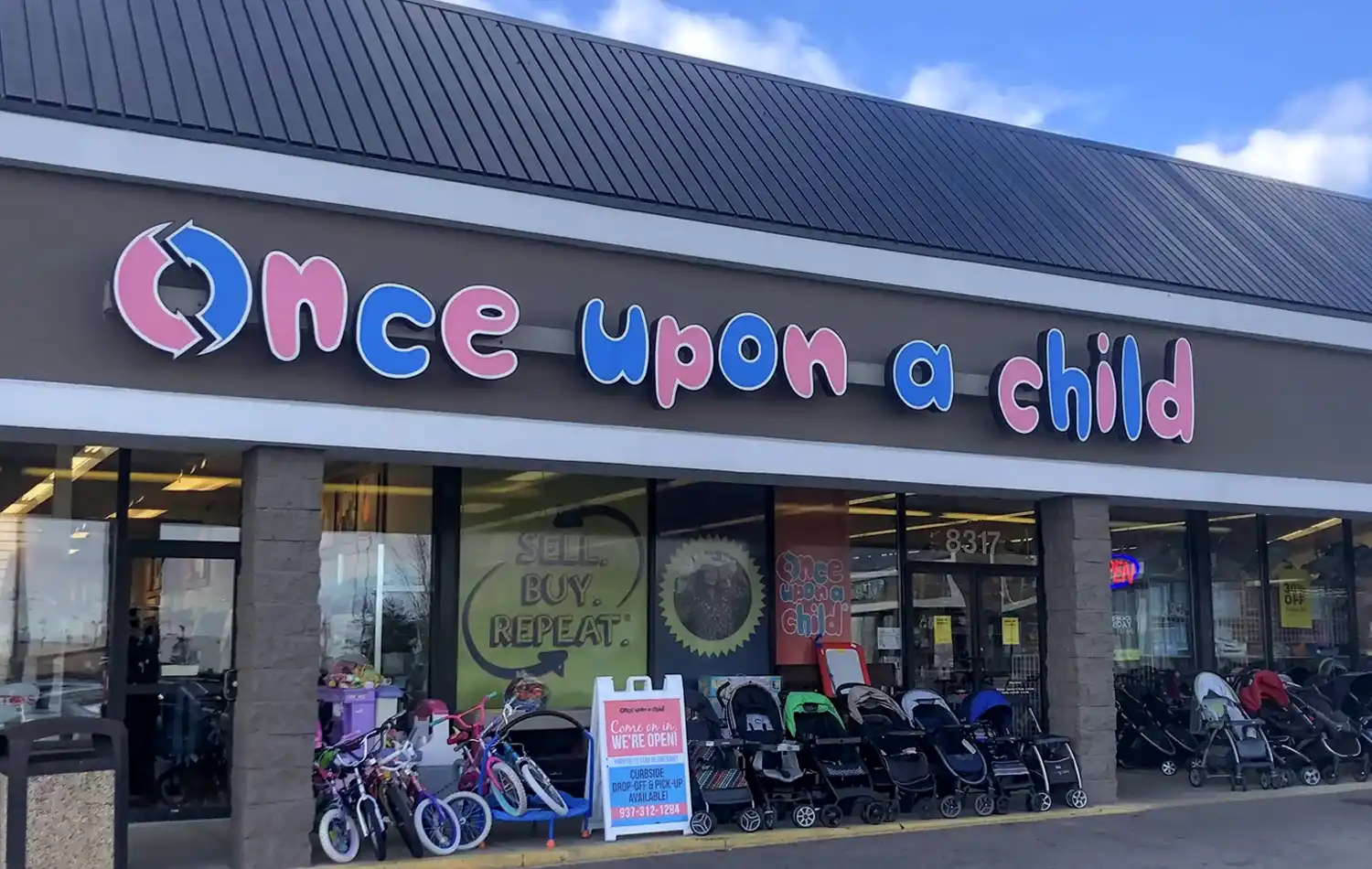 Exterior of a children's store named Once Upon a Child with a colorful sign and strollers and bicycles displayed outside.
