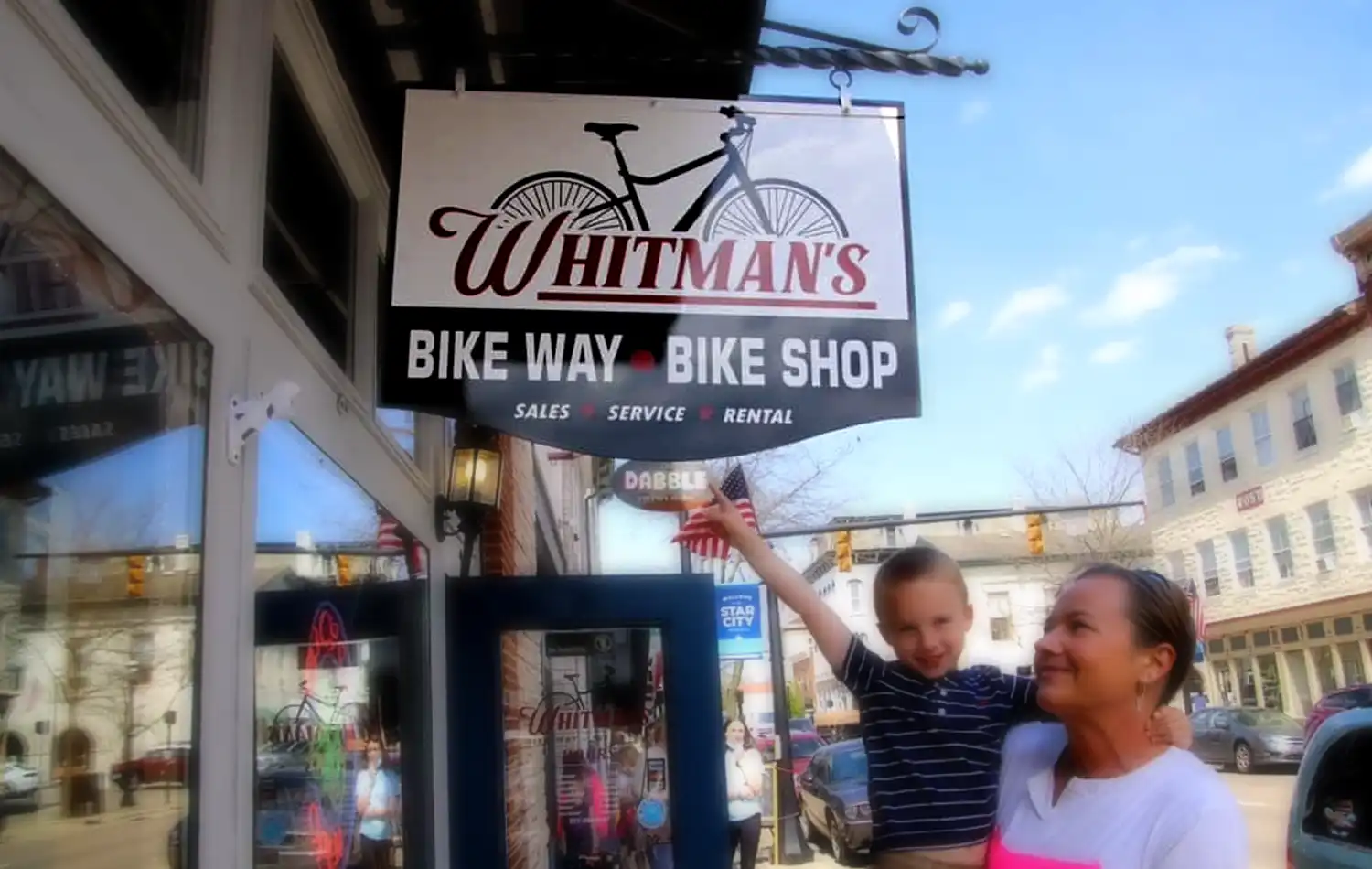 A man and a child pose outside Whitman's Bike Way bike shop sign.