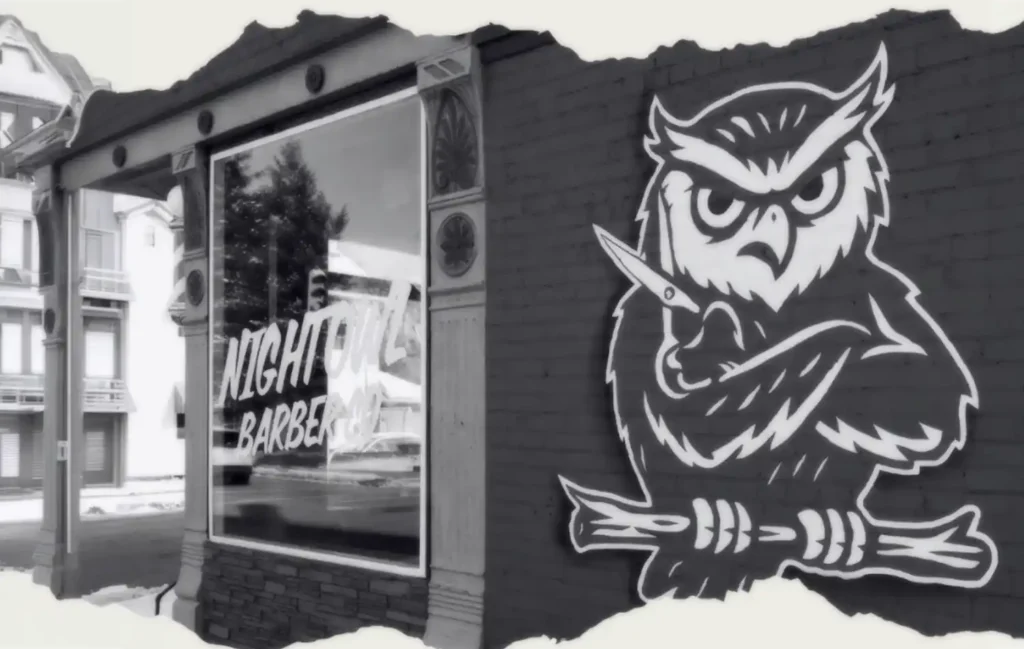 Graffiti mural of a large white owl perched on a branch on the side of a building beside a storefront window.
