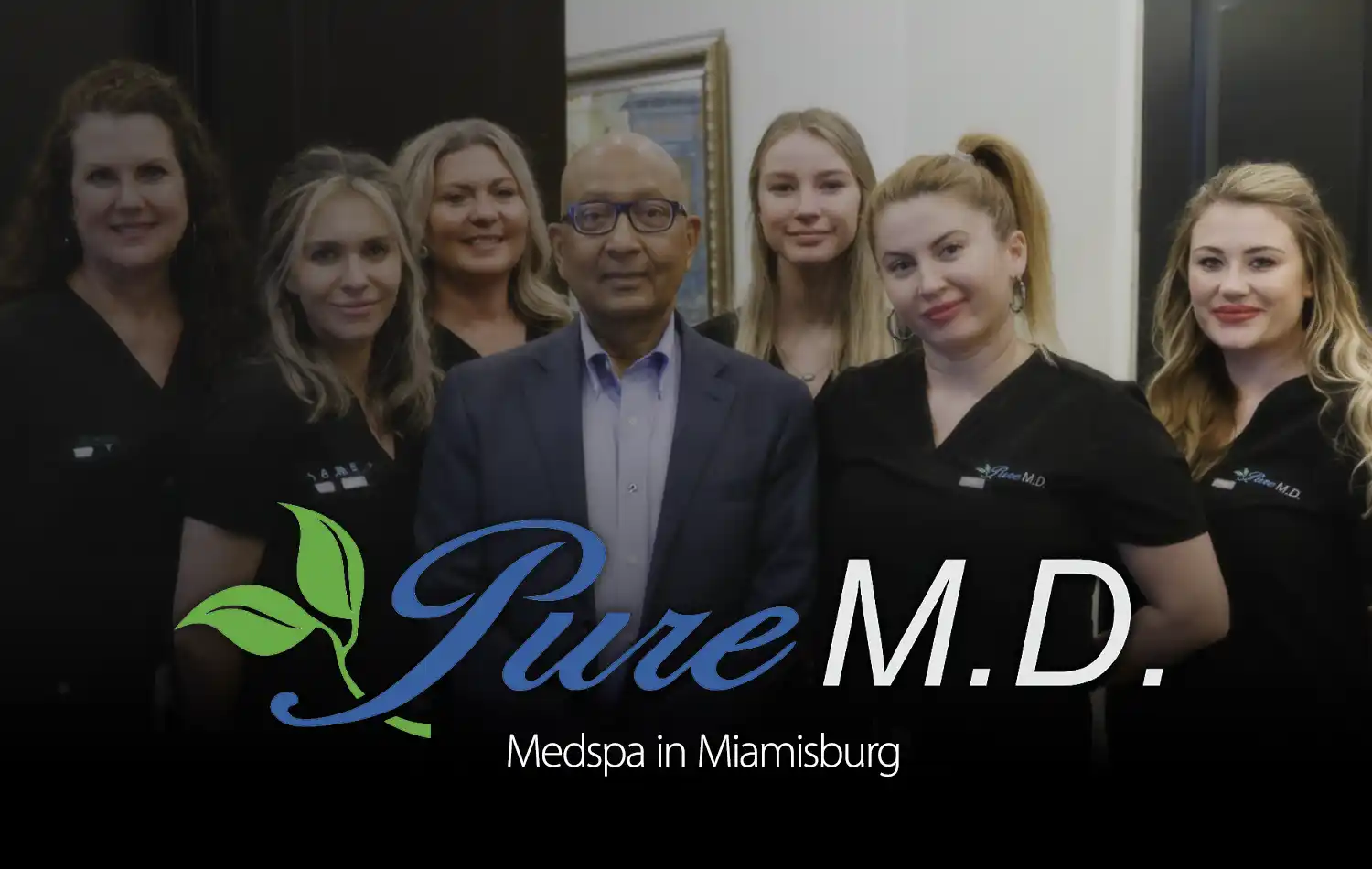 Group of medical spa staff posing for a photo, with a man in a suit center and the Pure M.D. logo visible.